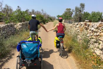 To syklister hånd i hånd - sykkeltur på grusvei med barnevogn på slep